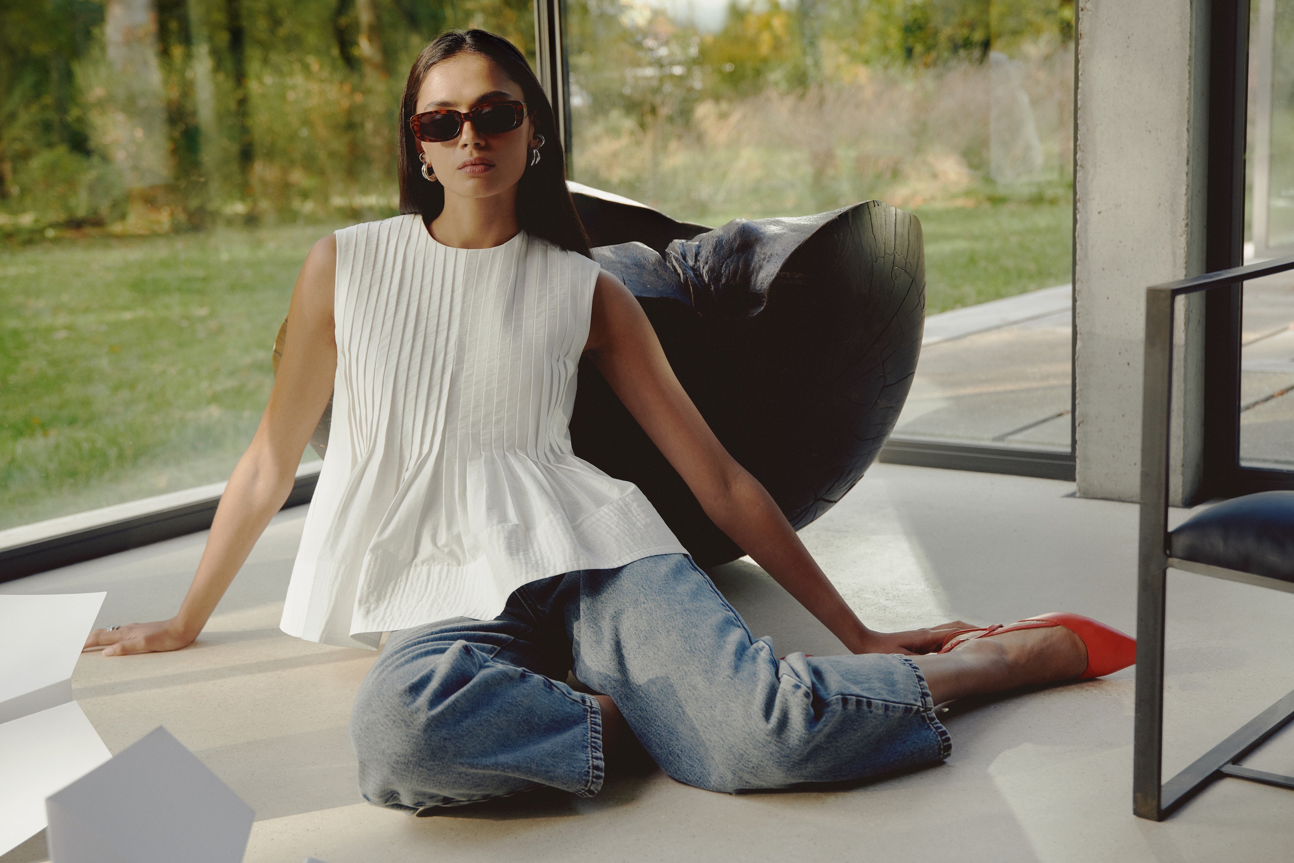 Woman sitting on a modern chair in a bright room with large windows.